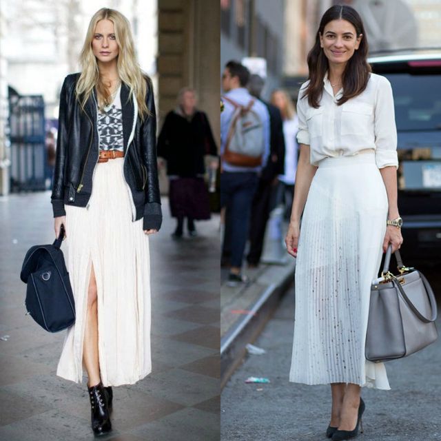 Woman wearing a black graphic t-shirt, beige pleated maxi skirt, and black ankle boots with a brown belt and black handbag; woman in a white button-up shirt, white pleated maxi skirt, and gray handbag