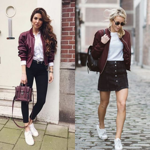 Woman wearing a burgundy bomber jacket, white shirt, black skinny jeans, and white sneakers, holding a burgundy handbag