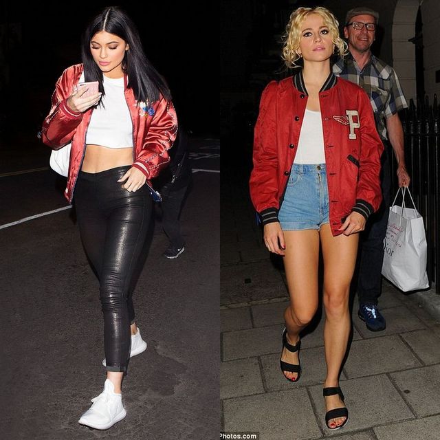 Woman wearing a red bomber jacket, white crop top, black leather leggings, and white sneakers, walking on a street