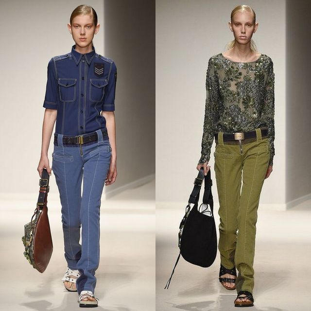 Woman wearing a blue button-up shirt, blue jeans and white sandals, holding a brown shoulder bag; woman in a green embellished top, olive green pants and black sandals, carrying a black bag