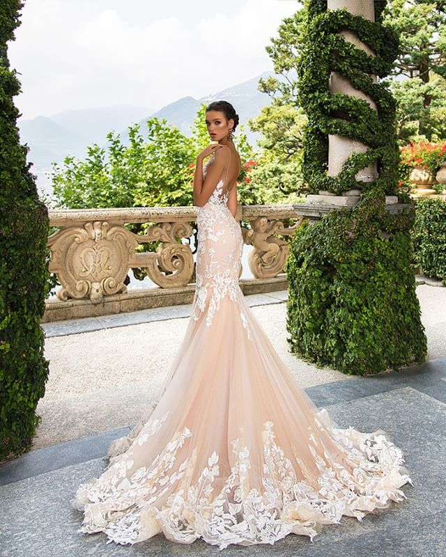Woman in a nude mermaid gown with floral lace detailing and a sheer train, standing in a garden setting