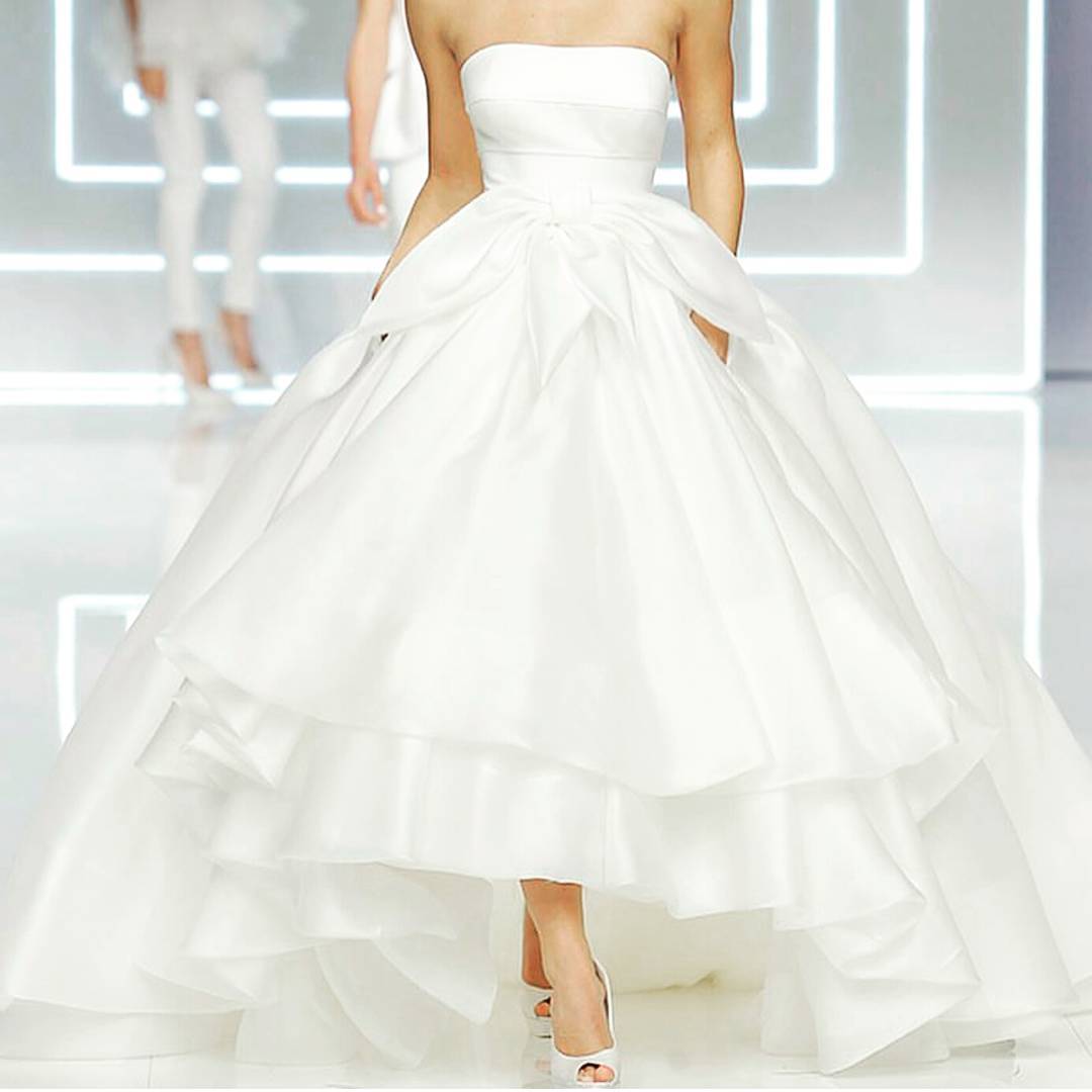 Woman in a white strapless ball gown with a large bow and layered skirt, paired with white heels