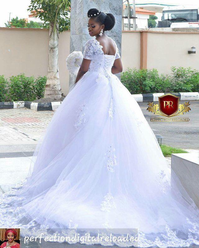 Woman in a white tulle ball gown with floral appliqués and short puff sleeves, holding a bouquet