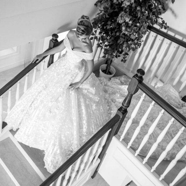 Woman in a white off-the-shoulder ball gown with a full skirt descending a staircase
