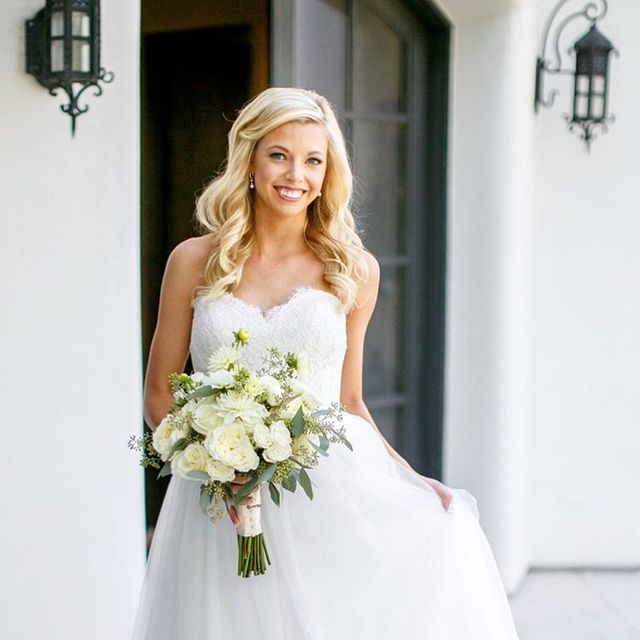 Woman in a white lace strapless wedding gown holding a bouquet of white flowers with greenery