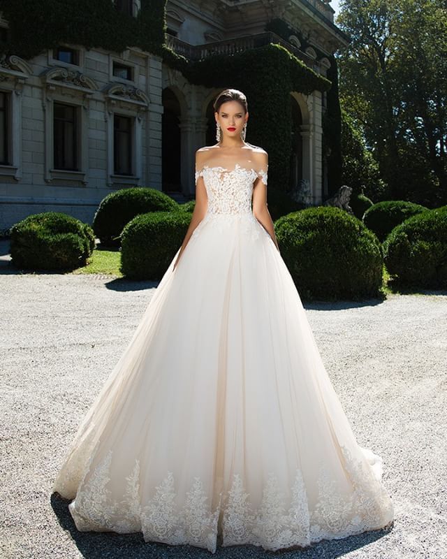 Woman in a cream ball gown with lace detailing and an off-the-shoulder neckline