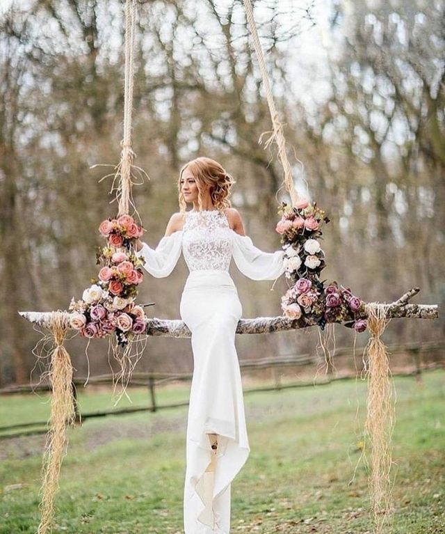 Woman in a white off-the-shoulder gown with a fitted bodice and a high-low hem, sitting on a floral swing