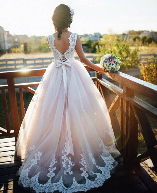 Woman in a light pink lace wedding gown with a fitted bodice and a full tulle skirt, holding a bouquet