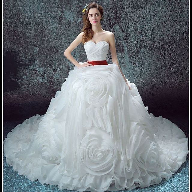 Woman in a white strapless ball gown with rose appliqués and a red satin belt
