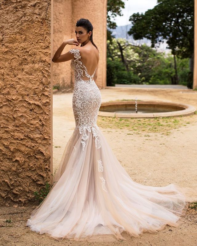Woman in a nude mermaid gown with lace detailing and a sheer train, standing outdoors