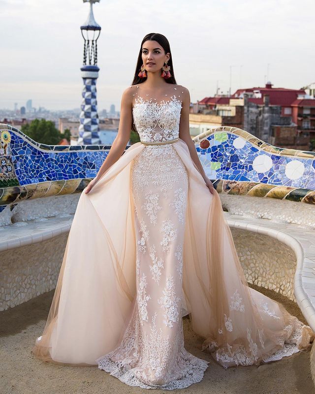 Woman in a nude lace gown with a fitted bodice, sheer overlay, and floral embellishments
