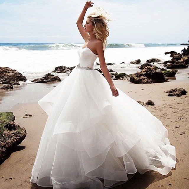 Woman in a strapless white tulle ball gown with a fitted bodice and layered skirt on a beach