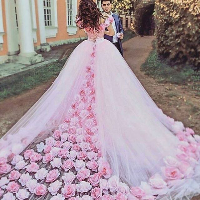 Woman in a pink tulle gown with a floral design and a long train, standing outdoors