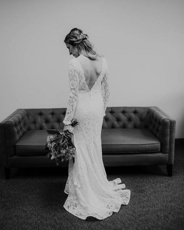 Woman in a white lace wedding dress with long sleeves and a low back, holding a bouquet of flowers