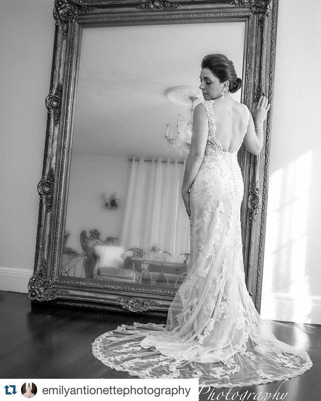 Woman in a lace wedding gown with a fitted silhouette and a long train, standing in front of a large mirror