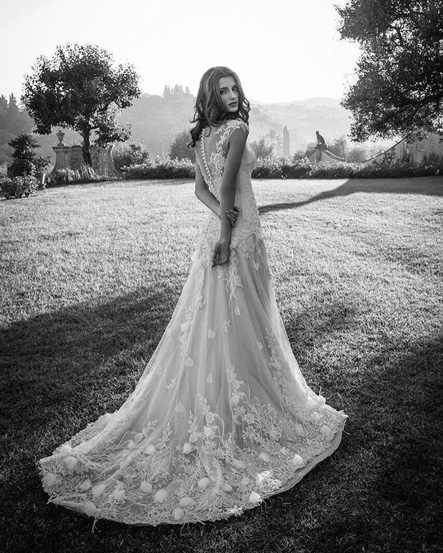 Woman in a white lace wedding gown with a fitted bodice and flowing skirt, standing in a garden