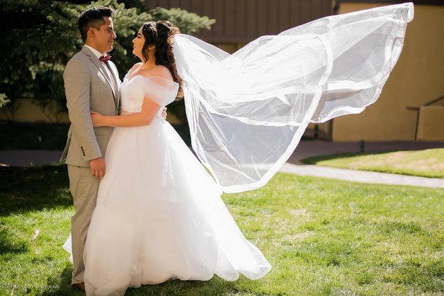 Woman in a white ball gown with a tulle skirt and a sheer veil, standing with a man in a light gray suit