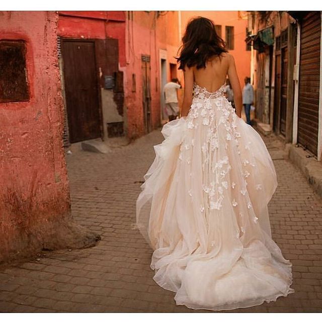 Woman in a cream tulle gown with floral appliqués and a fitted bodice, walking down a cobblestone street