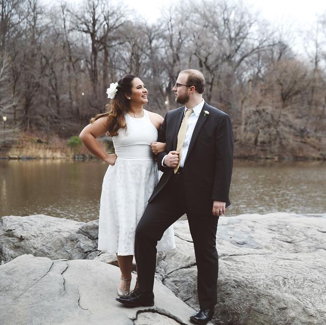Woman in a white lace fit-and-flare dress and silver strappy heels, standing beside a man in a black suit and tie