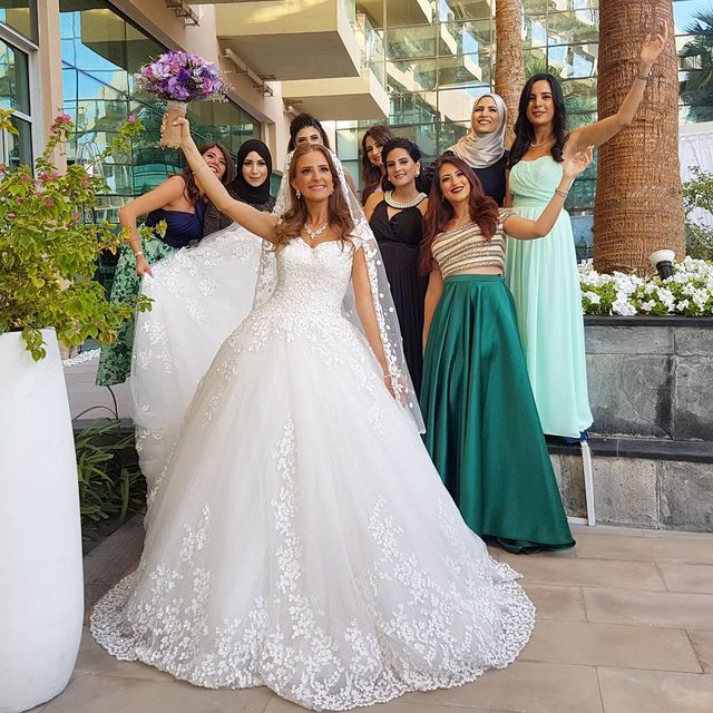 Woman in a white ball gown with lace detailing, surrounded by women in various long dresses in green, black, and pastel colors