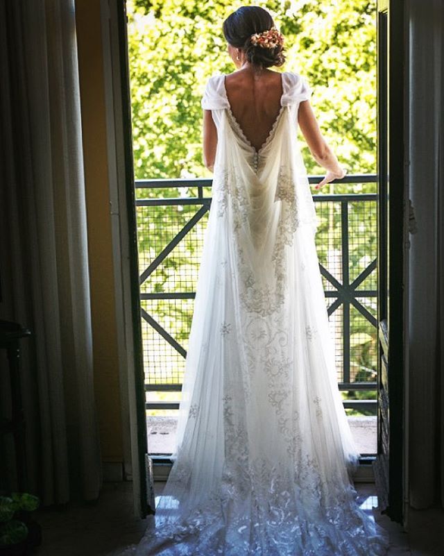 Woman in a white lace wedding gown with a deep V-back and flowing train, standing by a balcony