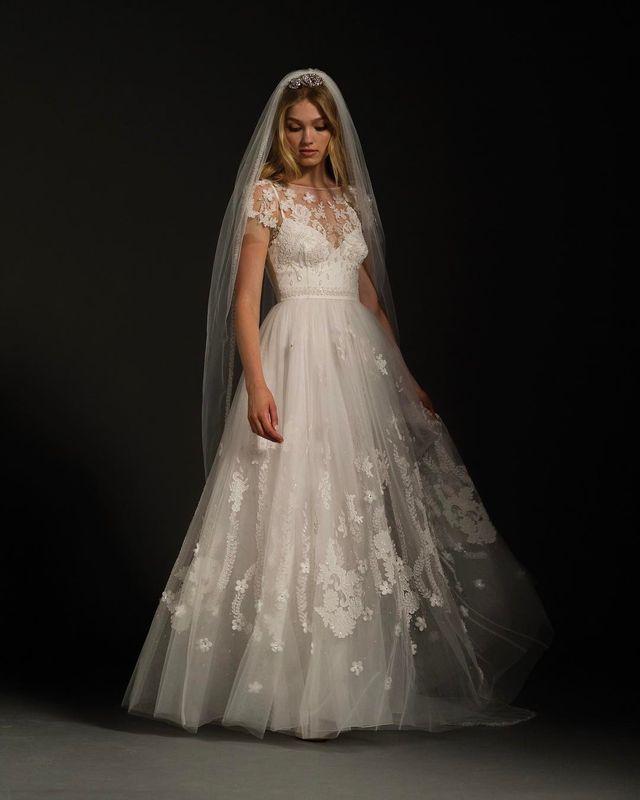Woman in a white lace wedding gown with a fitted bodice and flowing tulle skirt, wearing a long veil
