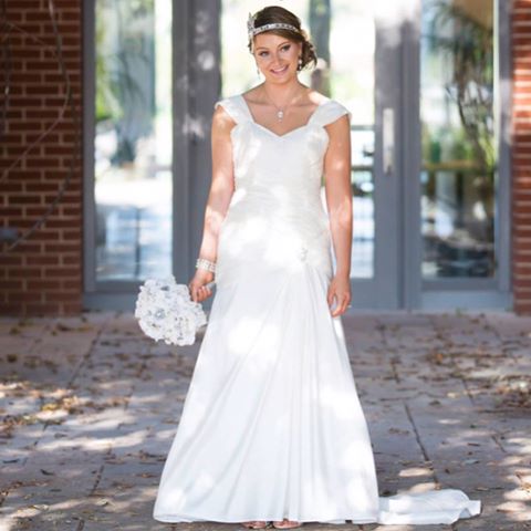 Woman in a white wedding gown with cap sleeves and a fitted bodice, holding a bouquet of white flowers