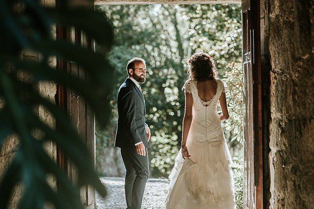 Woman in a white lace wedding dress with a fitted bodice and flowing skirt, standing in a doorway with a man in a black suit