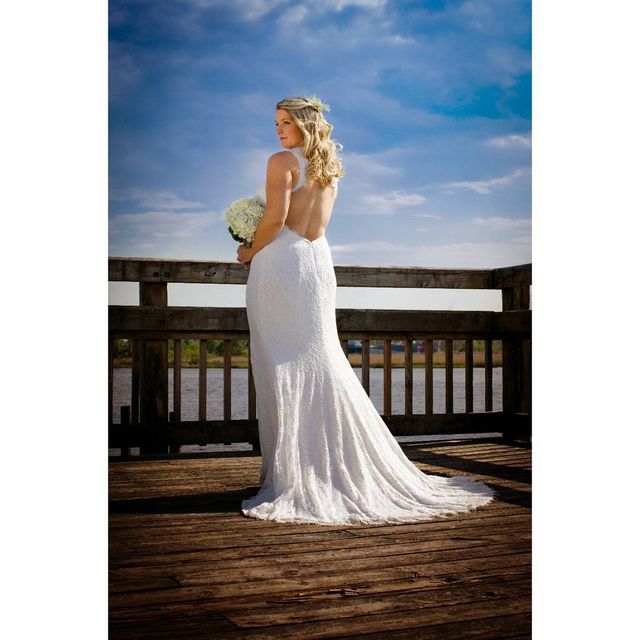 Woman in a white lace wedding gown with a low back, holding a bouquet of white flowers