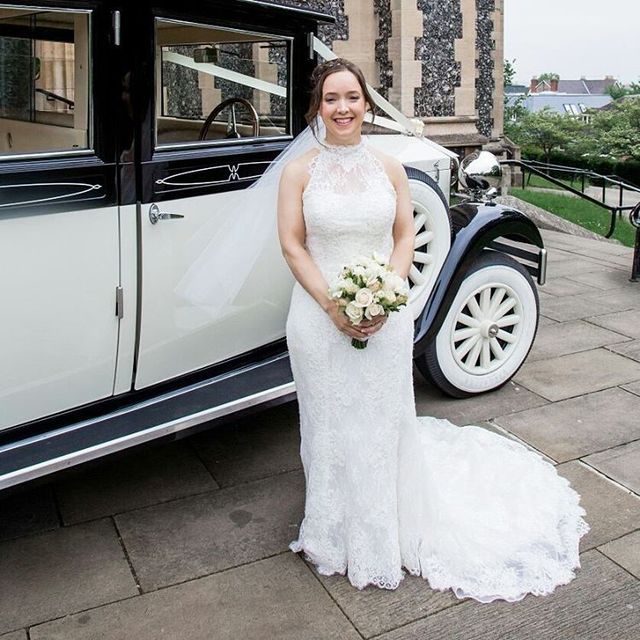 Woman in a white lace wedding dress with a high neckline and a long train, holding a bouquet of white flowers