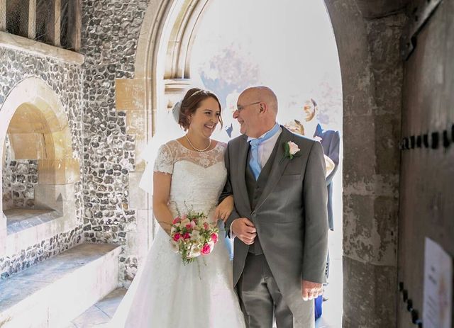 Woman in a white lace wedding dress with a fitted bodice and full skirt, holding a bouquet of pink flowers