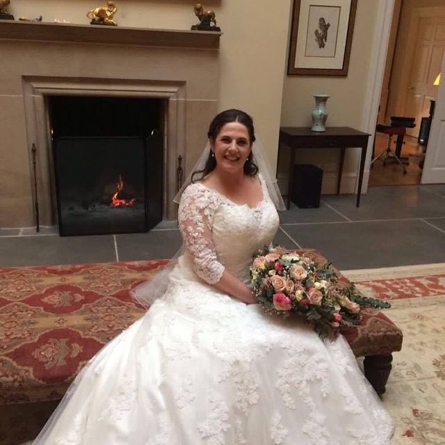 Woman in a white lace wedding gown with long sleeves, holding a bouquet of pink and cream flowers