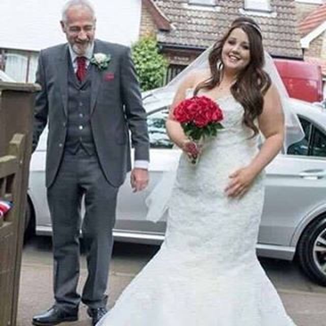 Woman in a white lace wedding gown with a mermaid silhouette, holding a bouquet of red roses