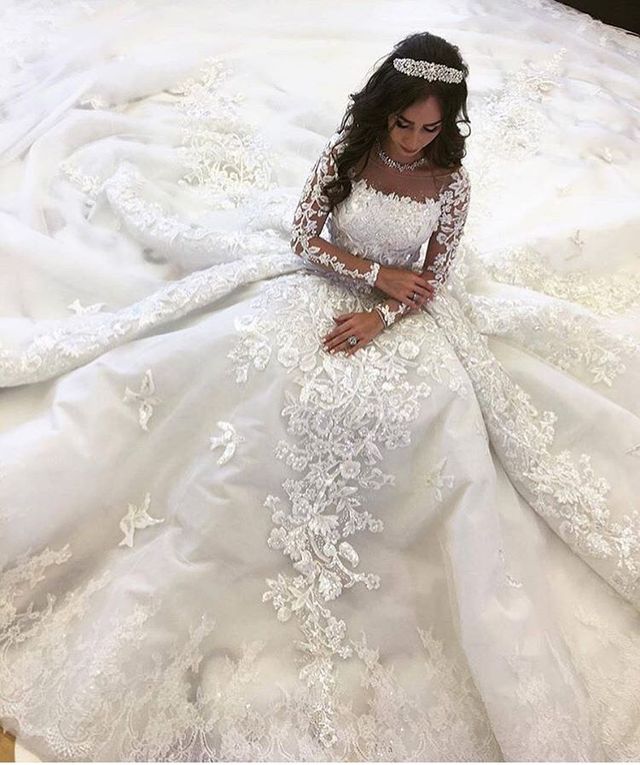 Woman in a white lace wedding gown with long sleeves and a full skirt, wearing a jeweled headband and bracelet