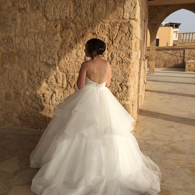 Woman in a white tulle ball gown with a fitted bodice and layered skirt, standing against a stone wall