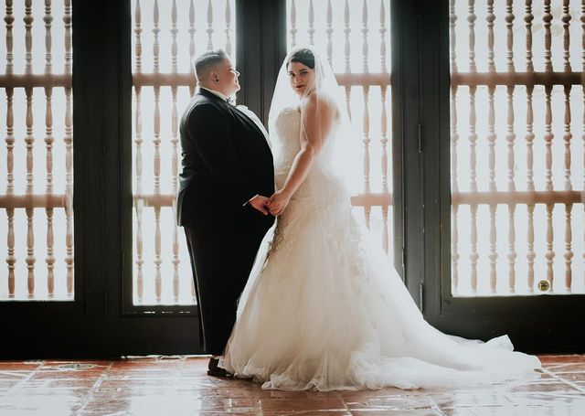 Woman in a white lace wedding gown with a fitted bodice and flowing skirt, holding hands with a person in a black tuxedo