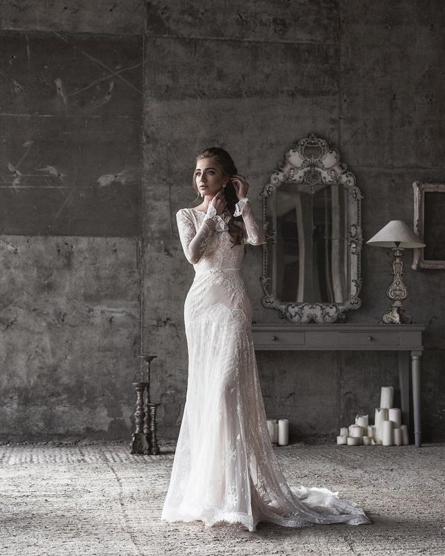 Woman in a white lace long-sleeve gown with a fitted silhouette and a flowing train in an industrial setting