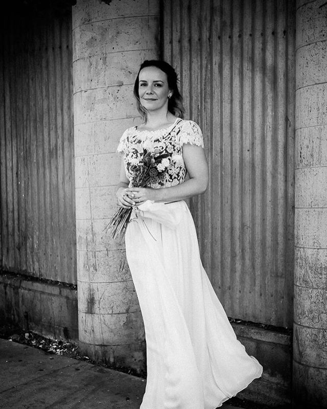 Woman in a white flowing gown with a floral lace top, holding a bouquet of flowers