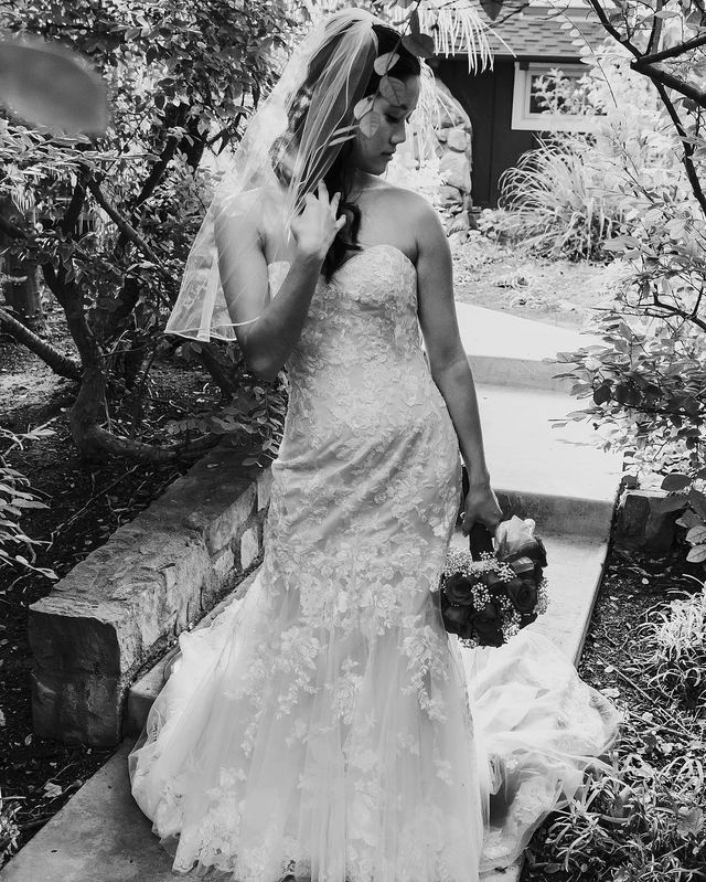 Woman in a white lace wedding gown with a fitted bodice and a flowing train, wearing a veil and holding a bouquet
