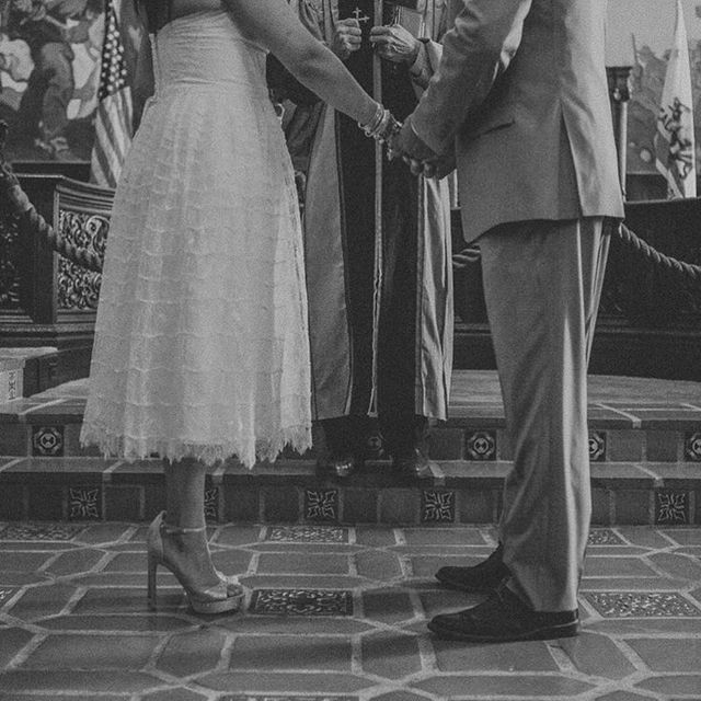 Woman in a white lace wedding dress and nude high-heeled shoes holding hands with a man in a gray suit