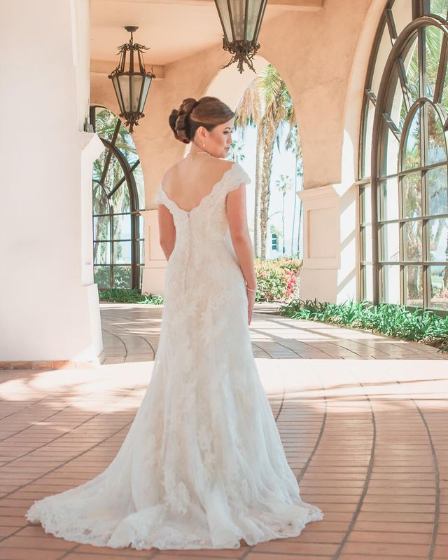 Woman in a white lace wedding gown with a fitted bodice and flowing train, standing in an arched corridor