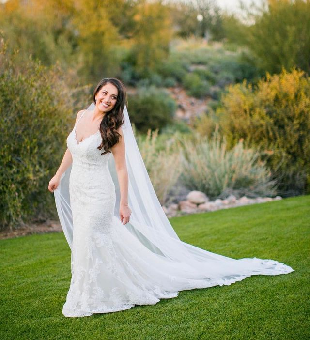 Woman in a white lace wedding gown with a long train and a flowing veil on a grassy landscape