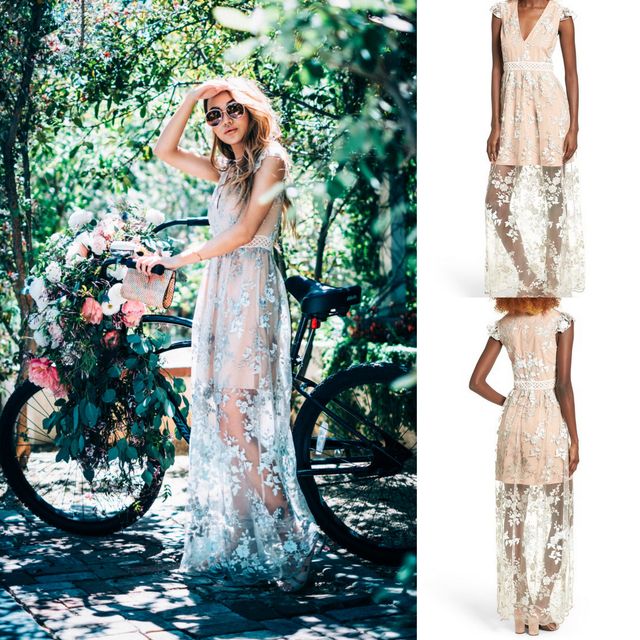 Woman wearing a sheer white floral maxi dress with cap sleeves and a cinched waist, standing next to a bicycle adorned with flowers