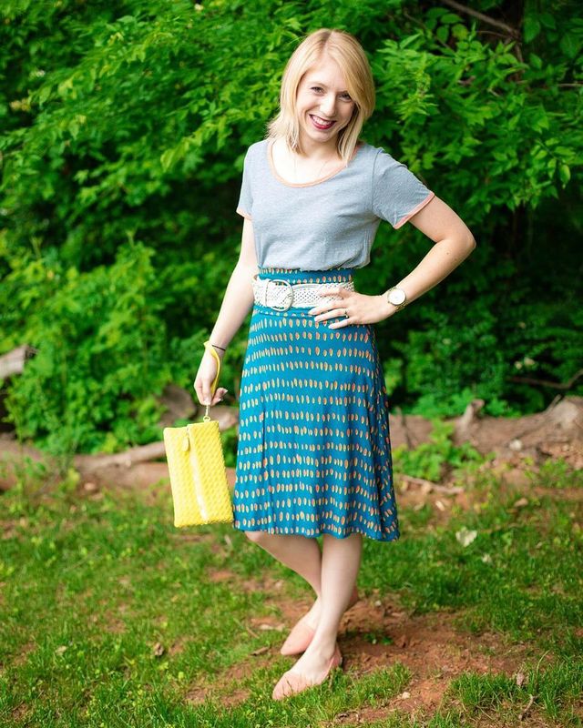 Woman wearing a gray t-shirt, blue patterned midi skirt, and nude flats, holding a yellow handbag