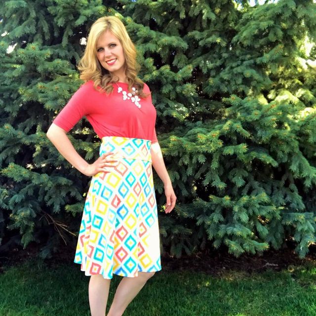 Woman wearing a coral top with short sleeves and a multicolored geometric print skirt