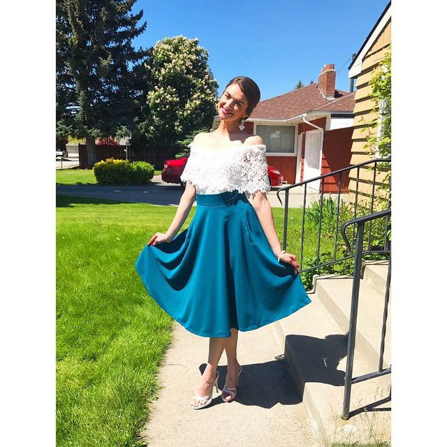 Woman in a white off-the-shoulder top and a teal midi skirt with silver strappy heels