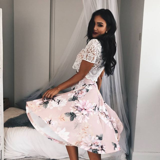 Woman wearing a white lace crop top and a pink floral midi skirt, twirling in a softly lit room