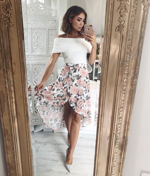 Woman in a white off-the-shoulder top and a pink floral high-low skirt with gray pointed-toe heels