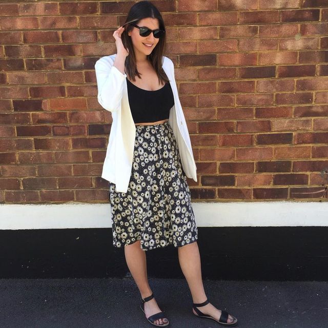 Woman wearing a white blazer, black crop top, and a black floral midi skirt with black sandals