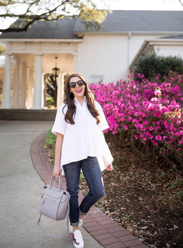 Woman wearing a white oversized button-up shirt, dark blue skinny jeans, and white sneakers, carrying a light gray handbag